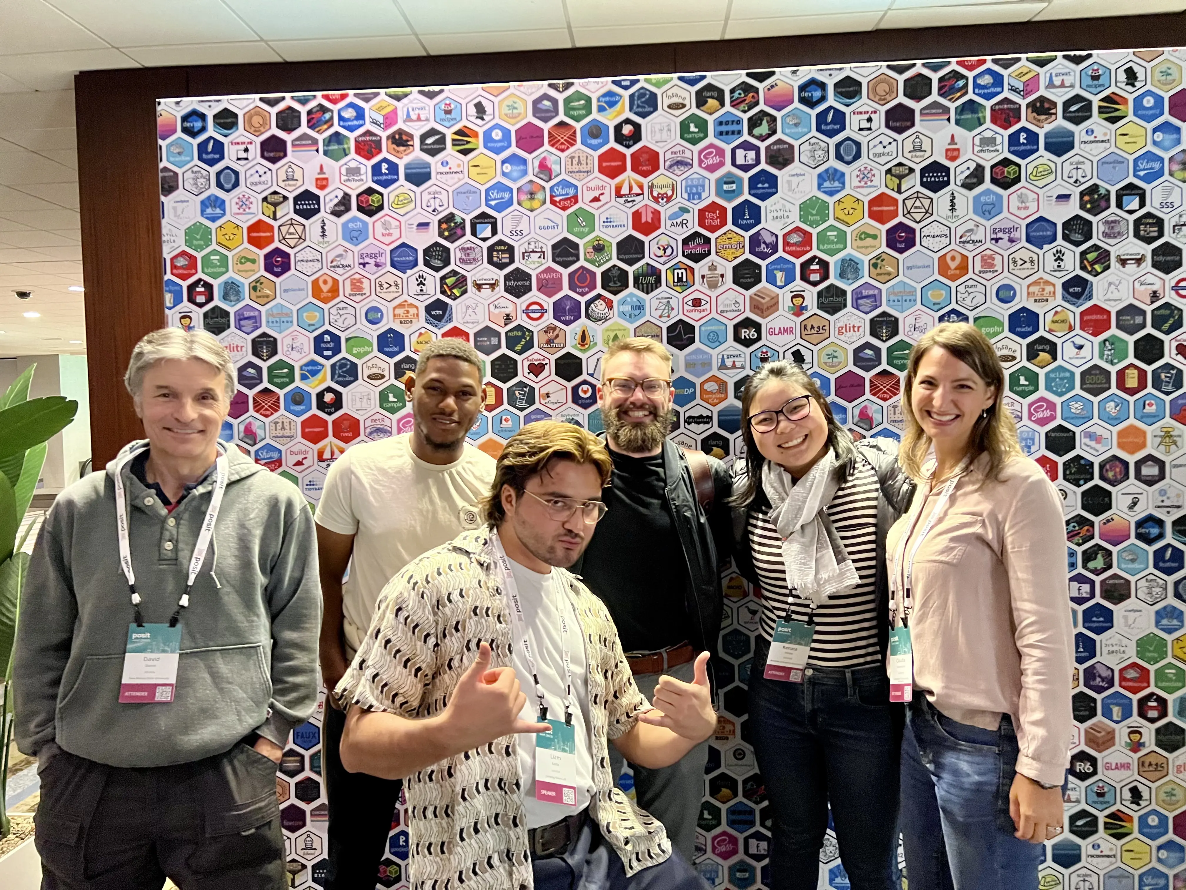 A group of six people smiling with a backdrop illustrated with hex stickers